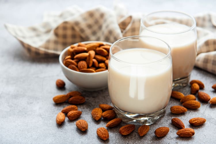 Two glasses of almond milk next to almonds and a cloth 