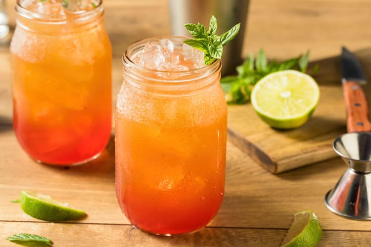 Two planter’s punch surrounded by lemon wedges and a shot pourer