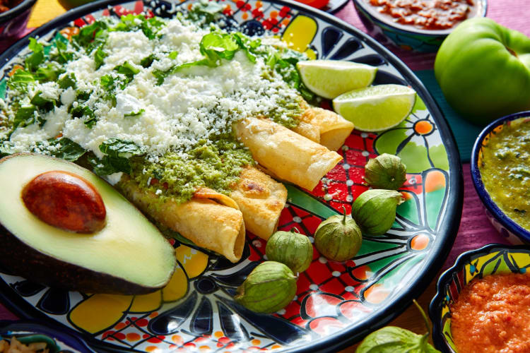 A plate of enchiladas verdes with avocado and sauces