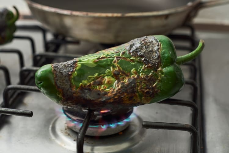 A poblano pepper being roasted on the stove