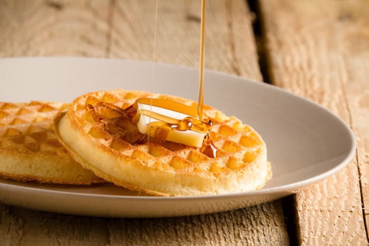 Two waffles with butter on top and honey being poured over as part of the best breakfast in Orange County