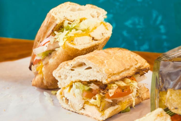 A sandwich with salad, chicken and melted cheddar cheese