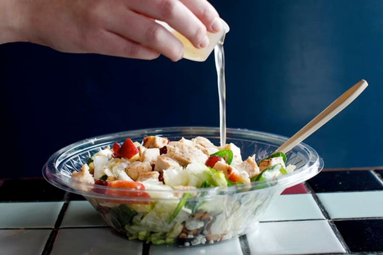 A person pouring dressing onto a Potbelly salad
