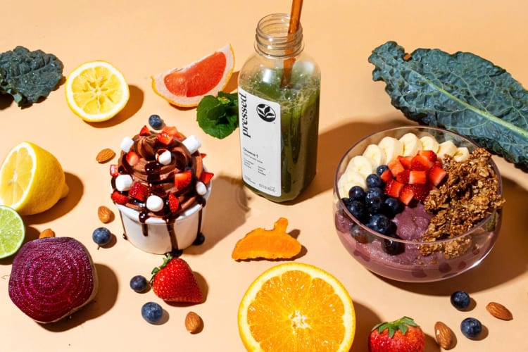 A juice, acai bowl and frozen yogurt, surrounded by fruit, from Pressed Juicery