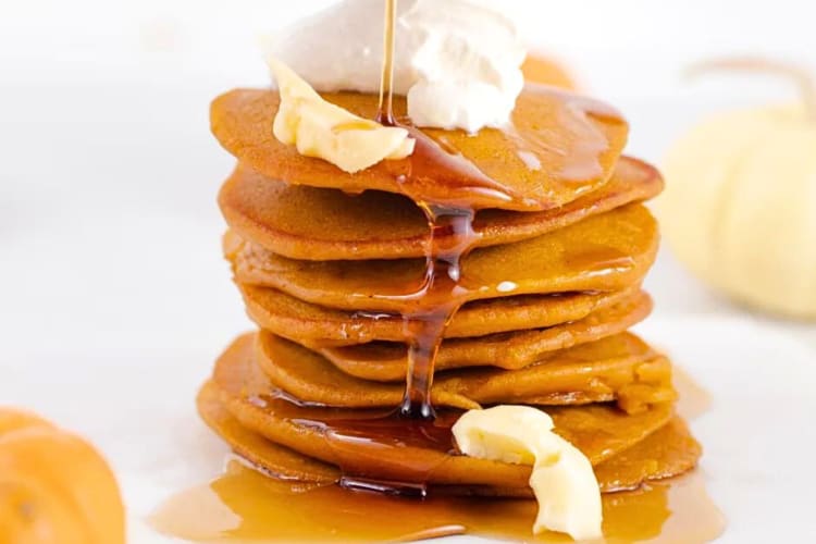 Stack of pumpkin pancakes, topped with cream, butter and syrup