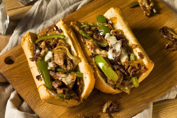 Two halves of a cheese steak sandwich with added green peppers