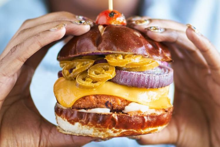 A person holding a veggie burger with cheese and jalapenos