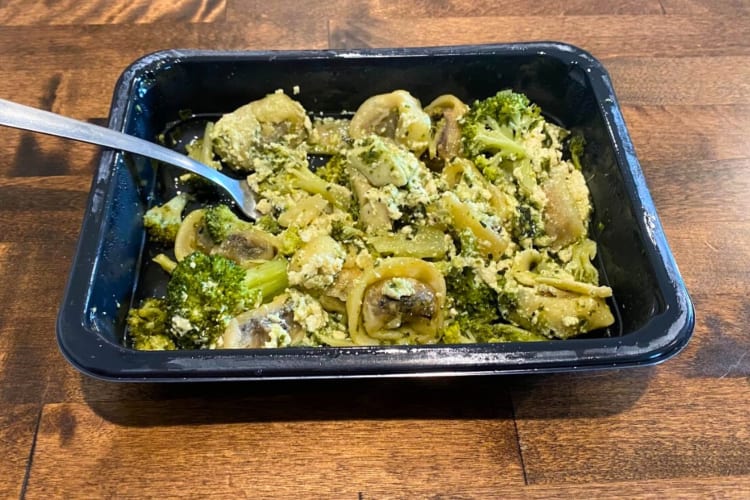 A plastic microwave container with pesto tortellini and broccoli 