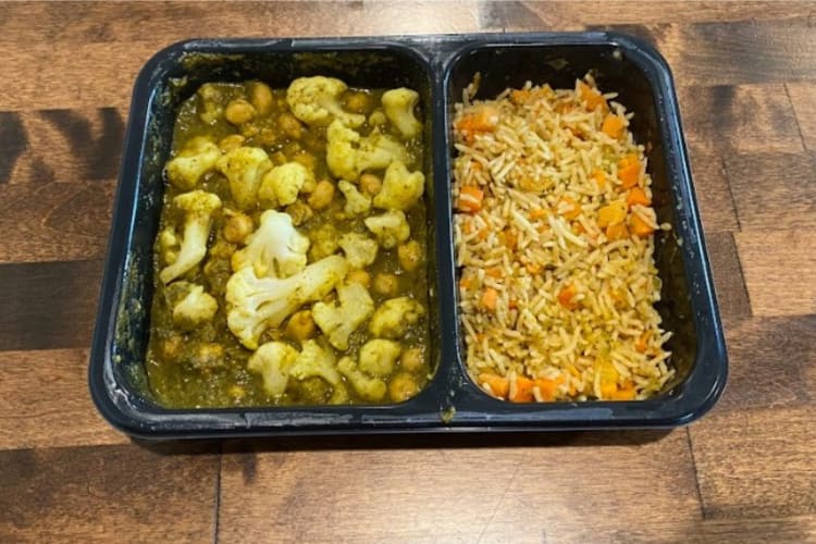 A black plastic microwave tray with califlower curry and rice