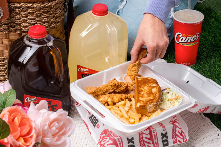 A person eating a Rasing Cane's meal on a picnic blanket