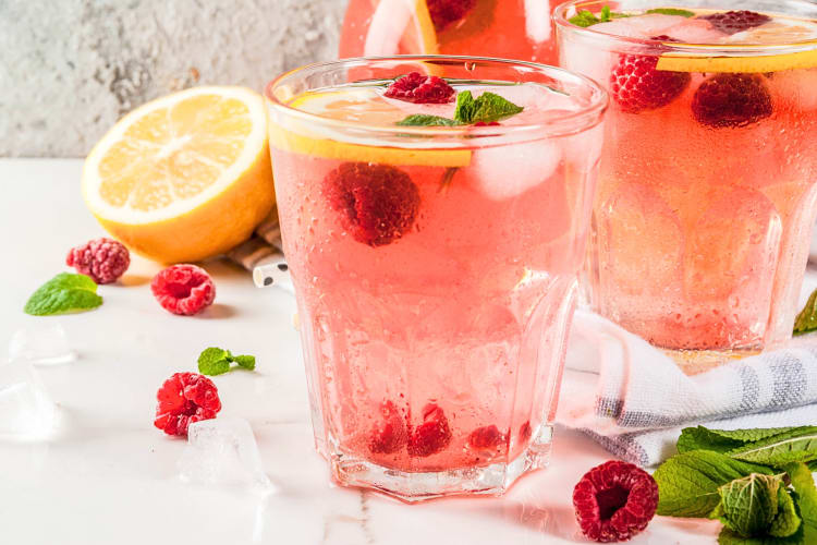 Two raspberry and lemonade vodka cocktails, surrounded by raspberries, lemon and basil 