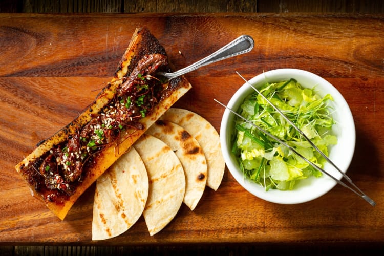 Aerial view of roasted bone marrow, four tortillas and lettuce shavings