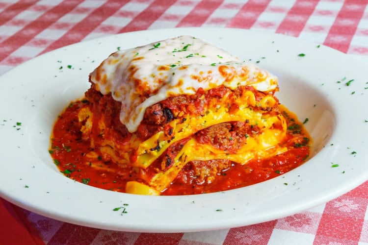 Lasagna on a plate on a table with a red and white tablecloth