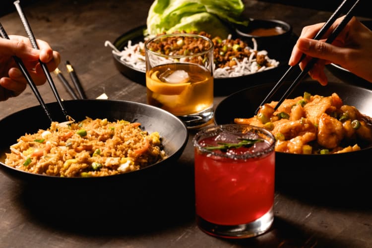 Black bowls with fried rice next to cocktails