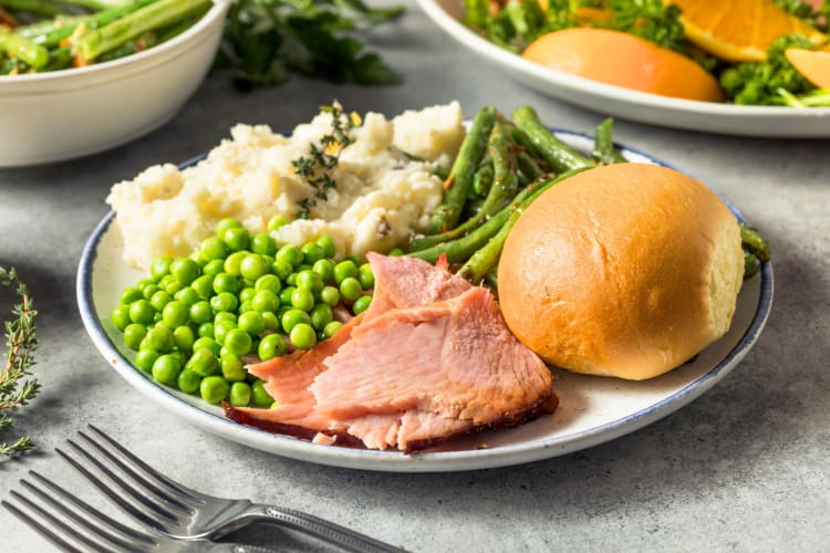 An Easter dinner plate with ham, mashed potatoes, green beans and a dinner roll
