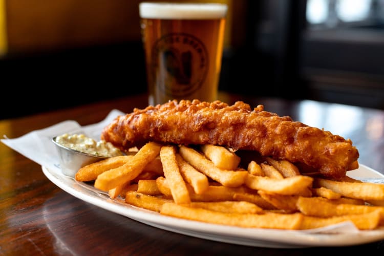 Fish and chips with tartar sauce next to a pint of beer