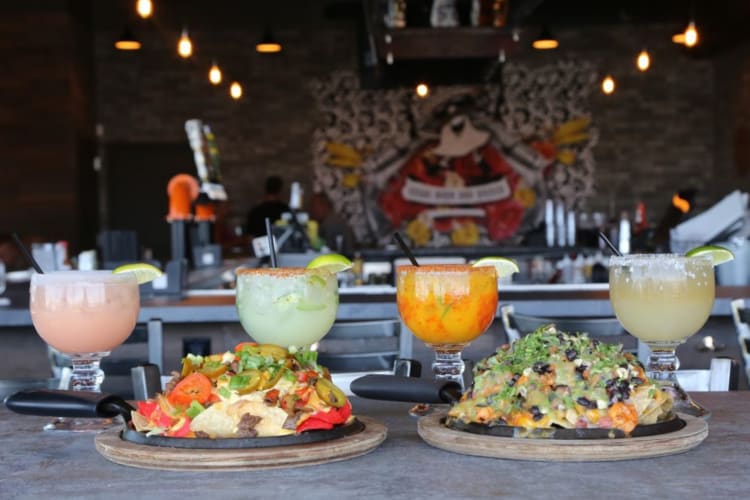 Two plates of nachos next to four colorful drinks