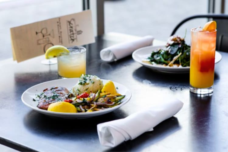 A menu next to two dishes and cocktails on a table