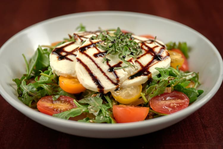 A caprese salad with greens, tomatoes and mozzarella in a bowl