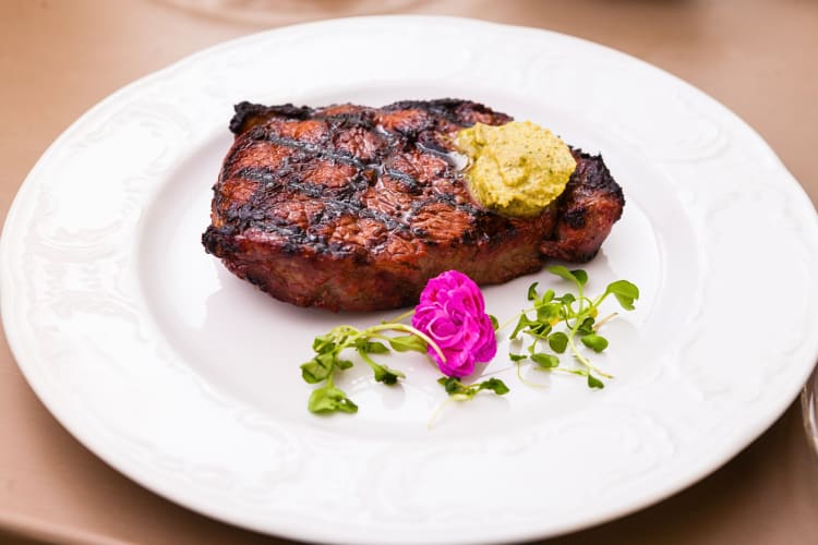 New York steak topped with butter, next to herbs and a flower on a plate