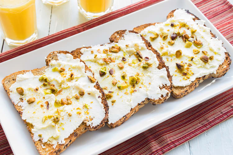 Three slices of toast topped with ricotta spread and crushed pistachios