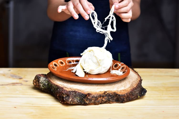 woman displaying stringiness of Oaxaca cheese