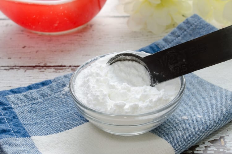 A measuring spoon in a glass bowl of baking powder — a cream of tartar substitute