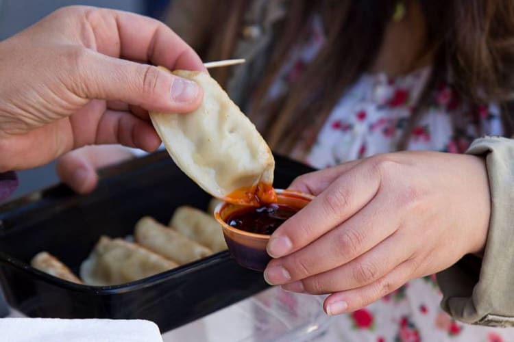 a hand dipping dumplings into a sauce on a Chinatown food tour