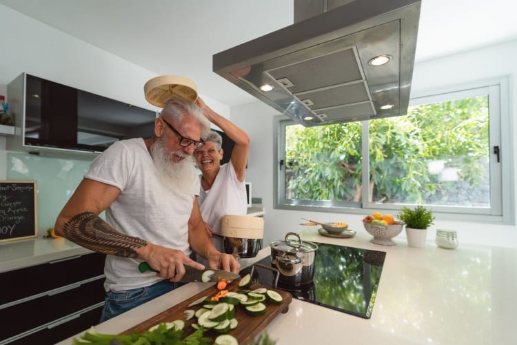 senior-aged couple laughing and cutting vegetables