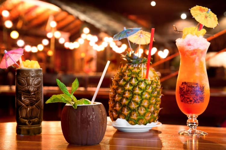 four Tiki-style drinks in a row, one served in a pineapple