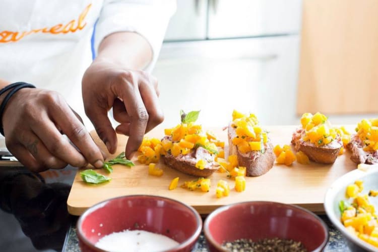 a chef in a Cozymeal apron spooning preparing herbs for appetizers