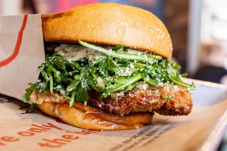 a breaded chicken sandwich with greens and sauce