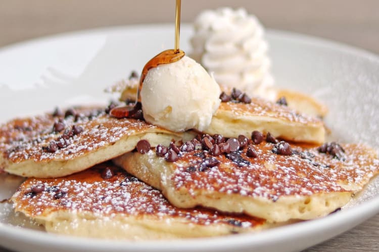 syrup being poured onto pancakes with whipped cream and ice cream