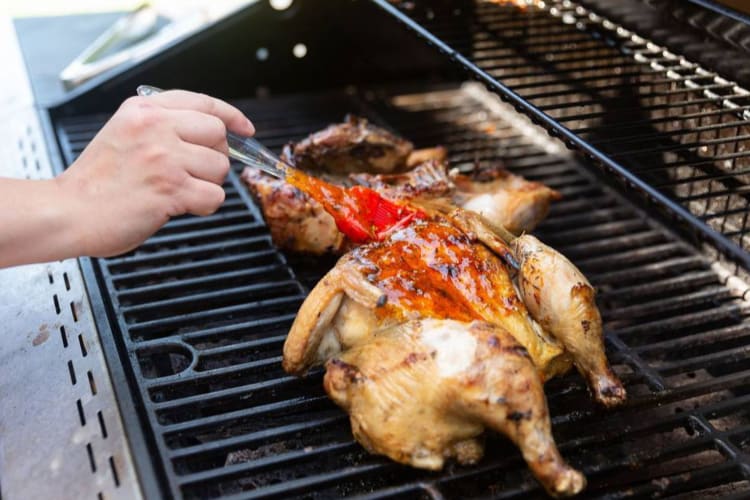 A hand basting sauce on a grilling chicken