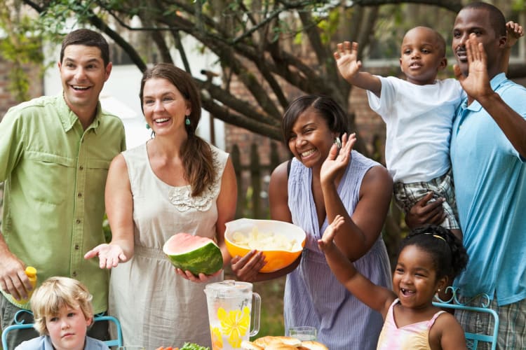 Two families waving at someone during a backyard cookout.