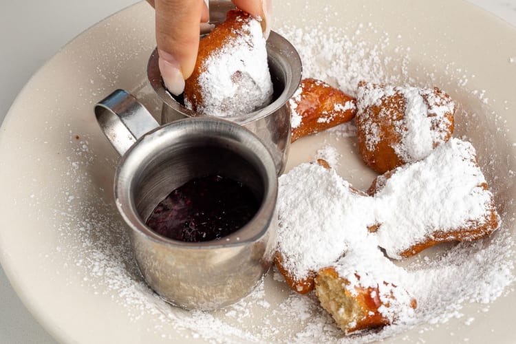 a woman dipping beignets into syrup