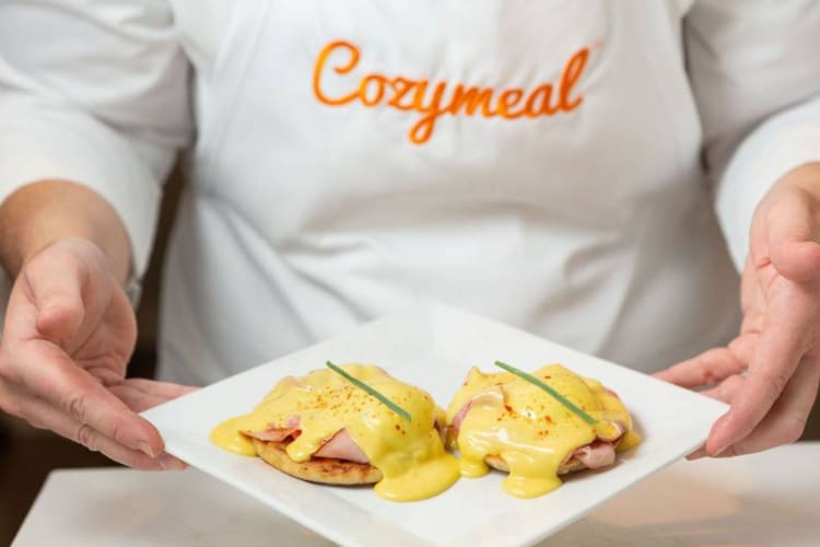 A chef showing a finished plate of eggs Benedict.