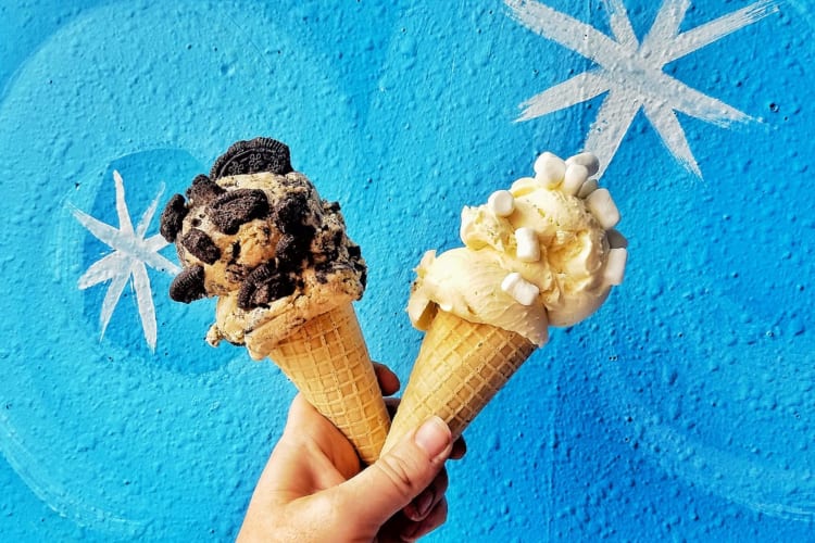 holding up two ice cream cones against a bright blue wall