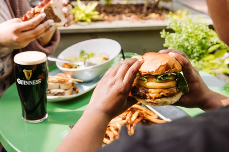 a man holding a huge burger, and a glass of Guinness beside him