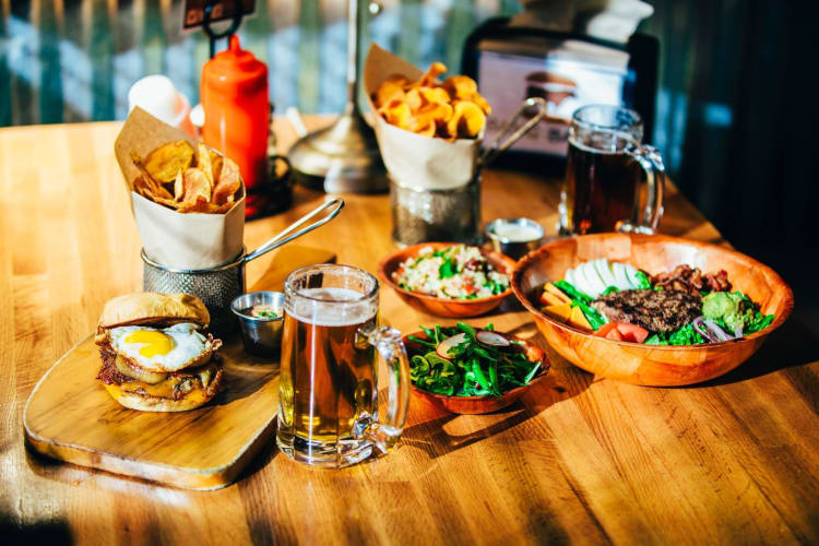 a spread of dishes including chips, beer, a burger and a steak salad