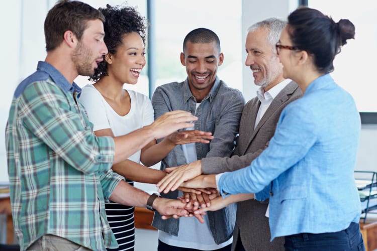 A group of four smiling co-workers putting all hands together