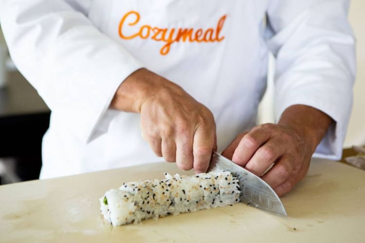 a chef in a Cozymeal apron cutting a sushi roll