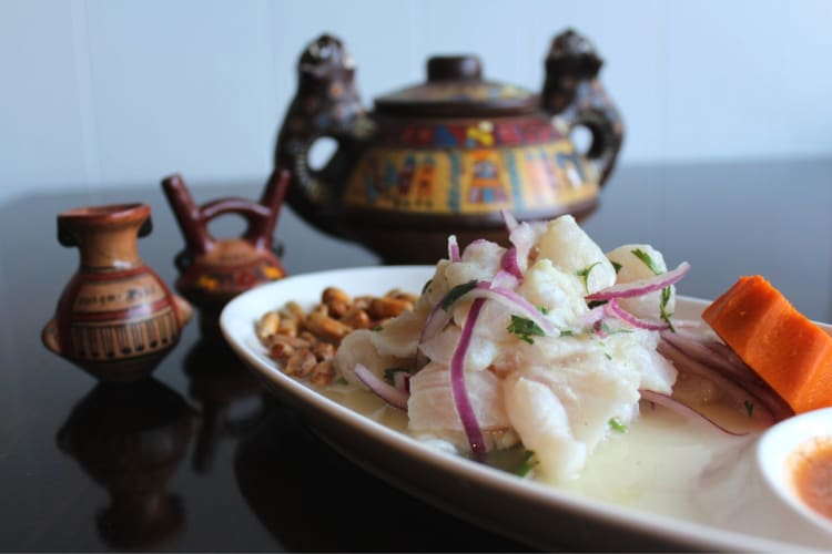 a dish of ceviche beside colorful traditional wooden art 