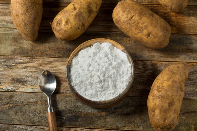 Potatoes and a spoon surrounding a bowl of potato starch — a great cornstarch substitute