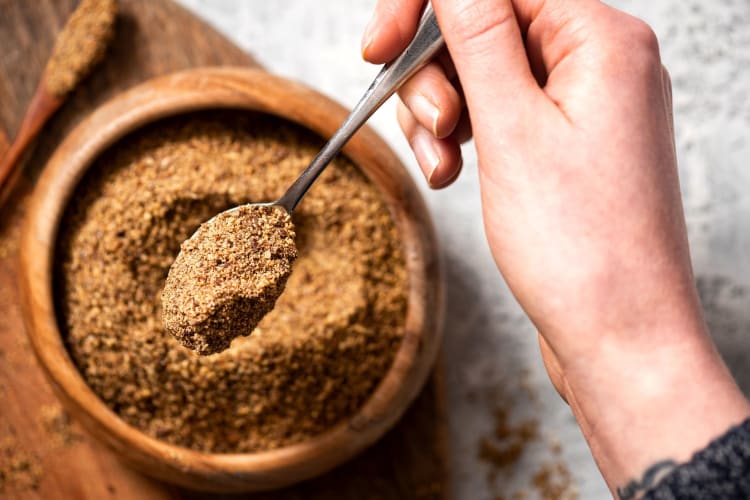 A hand lifting up ground flaxseed from a bowl, with a spoon