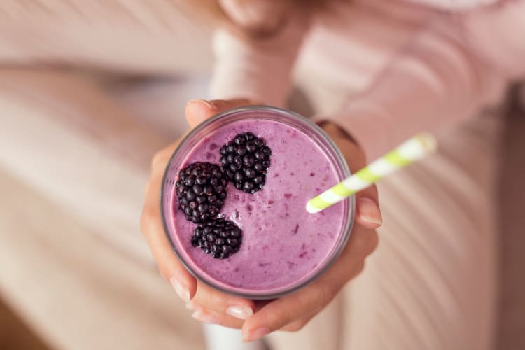 Hands holding a frozen berry smoothie topped with three blackberries