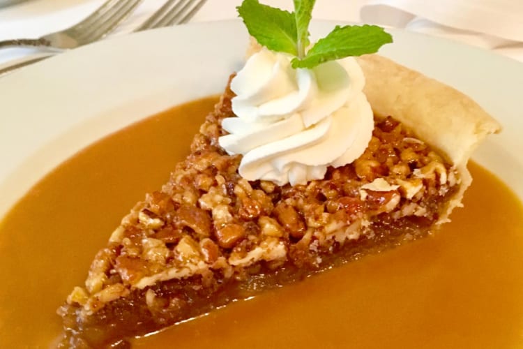 A slice of pecan pie with whipped cream and caramel sauce