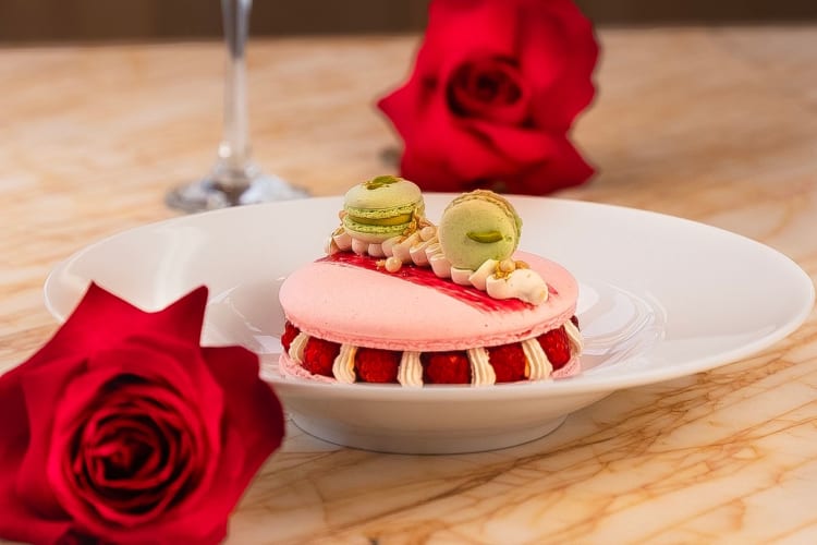 A fancy pink macaroon dessert next to red roses