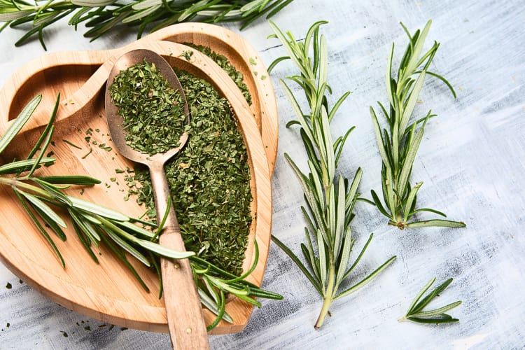 Aerial view of rosemary plants, ground up rosemary, wooden bowls and a spoon