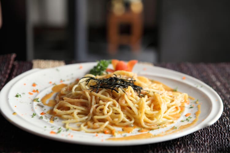 Mentaiko spaghetti dish on a white plate with garnish on top